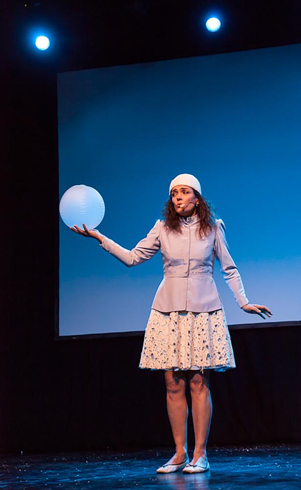 Eine Frau in einem Kostüm steht auf einer Bühne und hält einen Ballon.