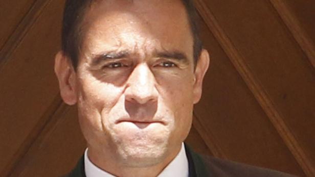 Porträt eines Mannes mit dunklen Haaren vor einem Holzhintergrund.