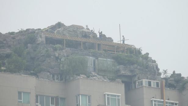 Auf dem Dach eines Wohnhauses befindet sich ein künstlicher Felsen mit einem Holzpavillon und mehreren Personen.