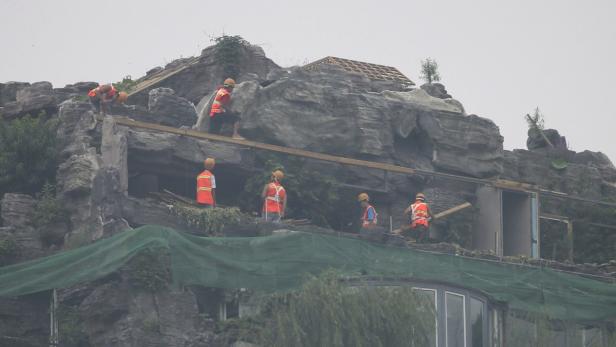 Mehrere Bauarbeiter arbeiten an einem Gebäude, das in eine Felsformation integriert ist.