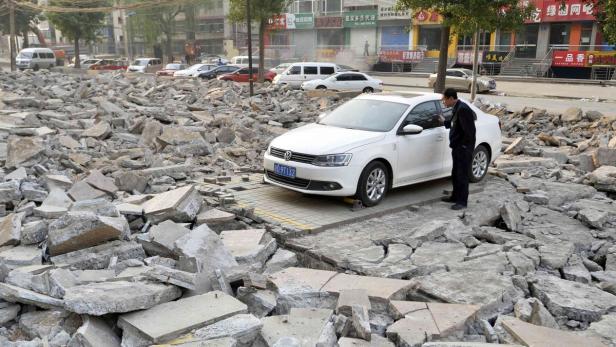 Ein Mann steht neben einem weißen Auto, das inmitten von Trümmern auf der Straße steht.