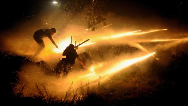 Zwei Personen zünden bei Nacht ein Feuerwerk mit langen, goldenen Funken an.