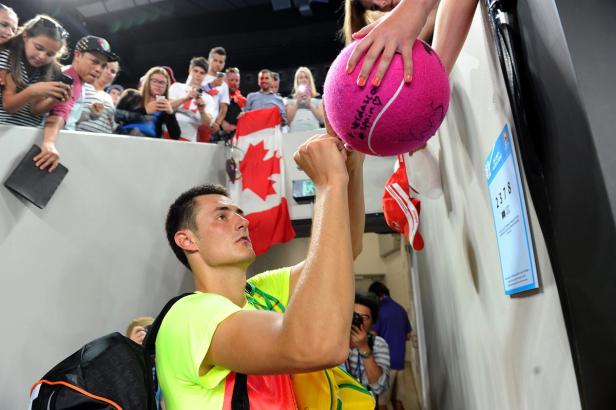 Ein Tennisspieler signiert einen pinkfarbenen Tennisball für Fans hinter einer kanadischen Flagge.