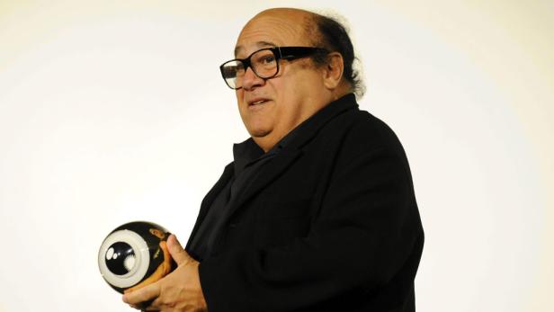 Danny DeVito hält eine große Augapfel-Skulptur.