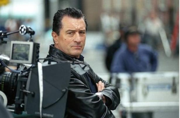 Robert De Niro steht mit verschränkten Armen hinter einer Filmkamera.