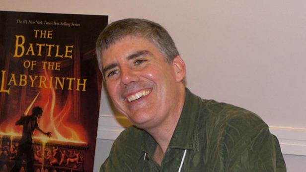 Rick Riordan posiert neben dem Buch „Die Schlacht im Labyrinth“.