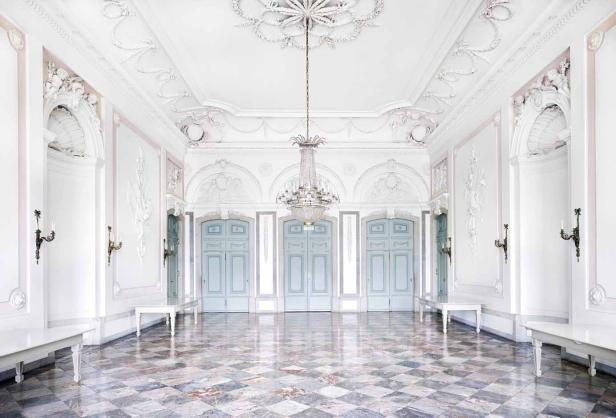 Ein leerer Ballsaal mit Marmorboden, weißen Wänden und einem Kristalllüster.