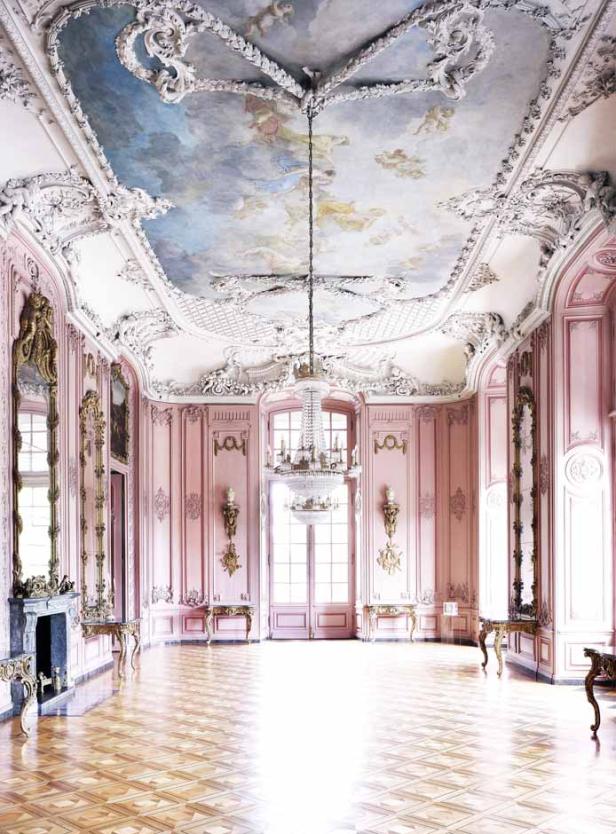 Ein prunkvoller Saal in Rosa mit Stuckdekor, einem Deckengemälde und einem Kristalllüster.