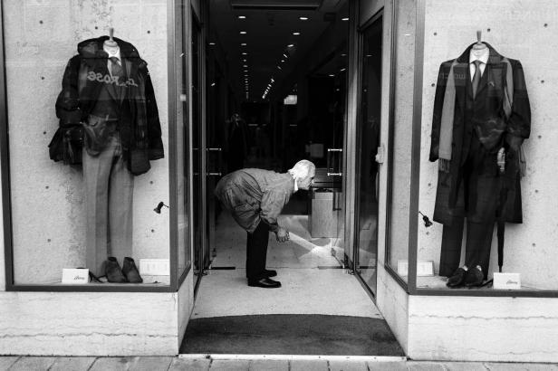 Ein älterer Mann beugt sich vor einem Schaufenster mit Herrenbekleidung.