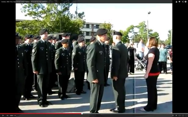 Ein Soldat macht seiner Freundin einen Heiratsantrag, unterstützt von seinem Zug.