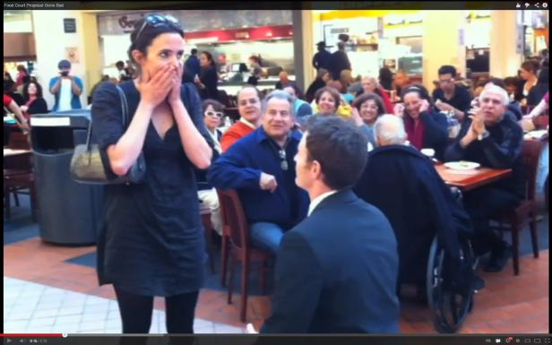 Ein Mann macht einer überraschten Frau in einem Einkaufszentrum einen Heiratsantrag.