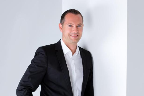 Ein Mann in Anzug und Hemd lächelt in die Kamera.