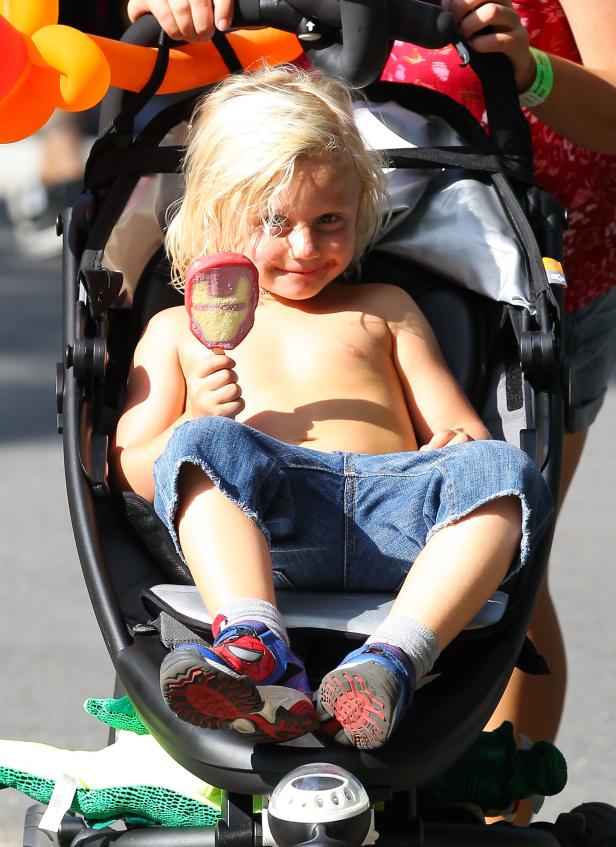 Ein barfüßiger Junge sitzt in einem Kinderwagen und hält ein Eis in Form von Iron Mans Maske.