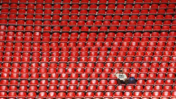Ein Mann sitzt inmitten leerer roter Sitze in einem Stadion und fotografiert.