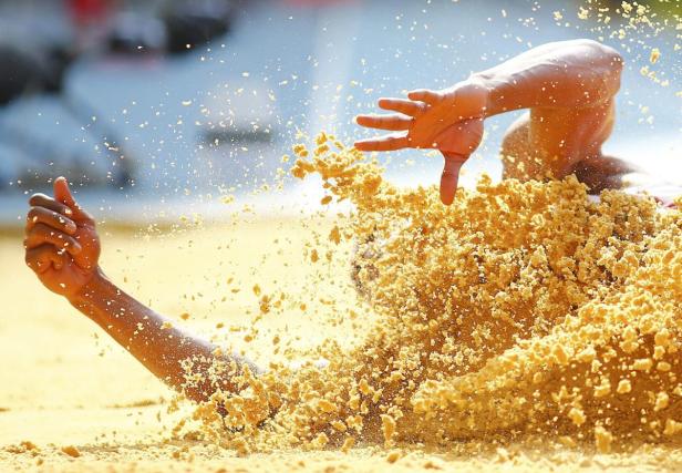 Ein Weitspringer landet in der Sandgrube, wobei der Sand aufwirbelt.