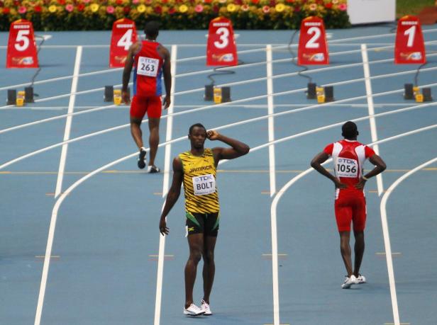 Usain Bolt steht auf einer blauen Laufbahn mit anderen Athleten im Hintergrund.