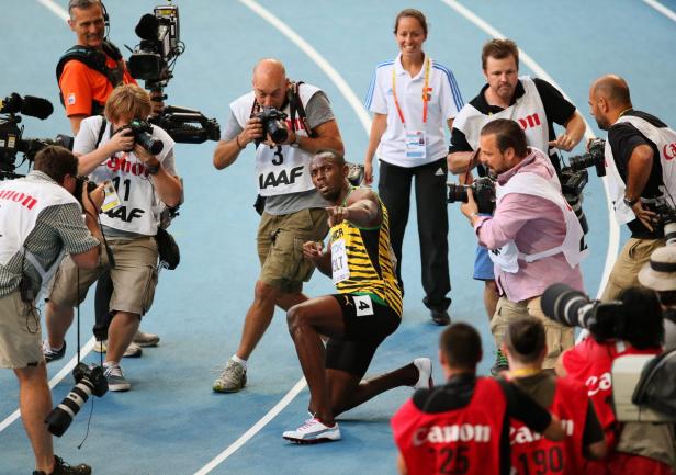 Usain Bolt posiert auf einer blauen Laufbahn, umringt von Fotografen.