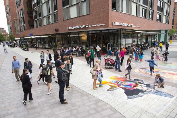 Menschen flanieren auf dem Lieblingplatz in Hamburg, wo ein 3D-Straßenkunstwerk zu sehen ist.