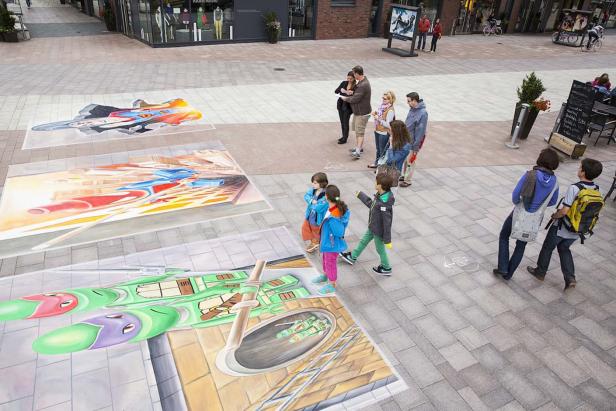 Menschen betrachten 3D-Straßenmalereien auf einem Platz.