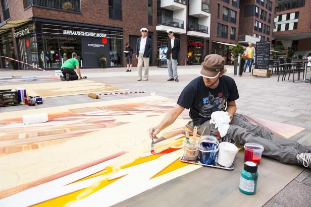 Ein Künstler malt ein großes Bild auf dem Boden einer belebten städtischen Fläche.
