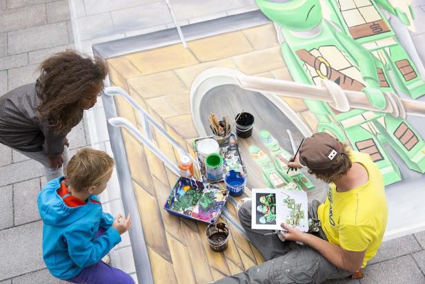 Ein Straßenmaler malt mit zwei Kindern ein 3D-Bild der Teenage Mutant Ninja Turtles.