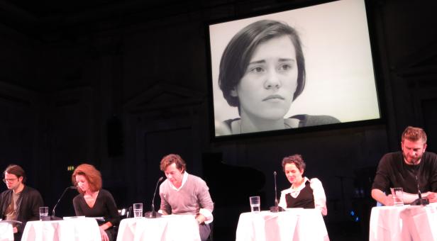 Eine Podiumsdiskussion mit fünf Personen vor einem großen Bildschirm mit einem Porträt.