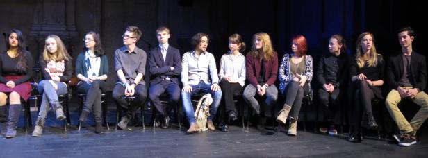 Eine Gruppe junger Leute sitzt auf Stühlen auf einer Bühne.