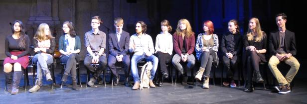 Eine Gruppe junger Leute sitzt auf Stühlen auf einer Bühne.