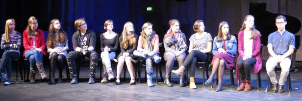 Eine Gruppe junger Leute sitzt auf Stühlen auf einer Bühne.