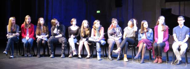 Eine Gruppe junger Leute sitzt auf Stühlen auf einer Bühne.