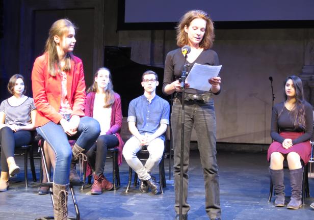 Eine Frau liest auf einer Bühne vor einem sitzenden Publikum.