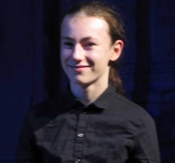 Ein junger Mann mit langen Haaren lächelt in die Kamera.