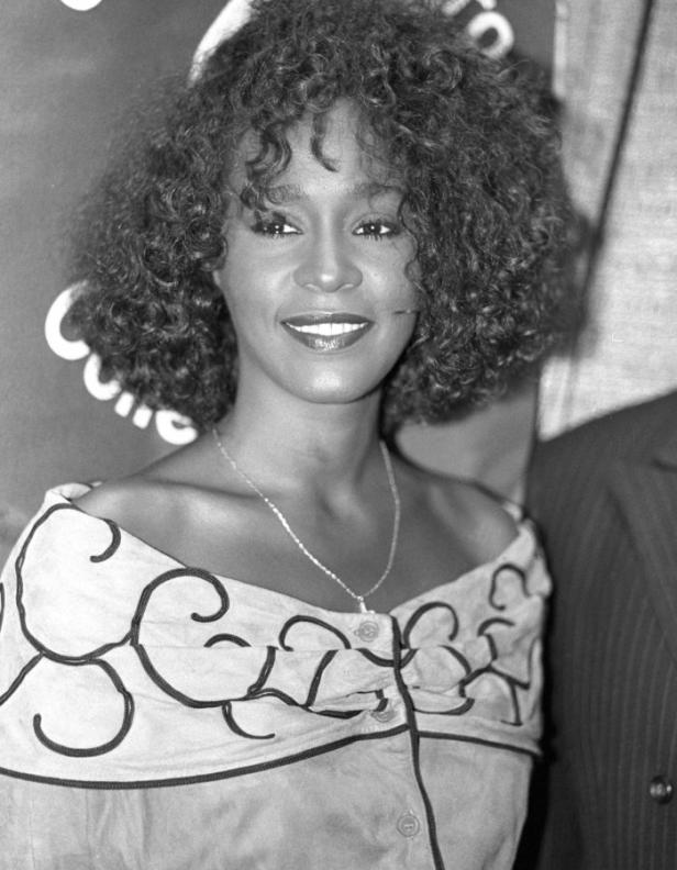 Ein Schwarzweißporträt von Whitney Houston mit lockigem Haar und einem gemusterten Oberteil.