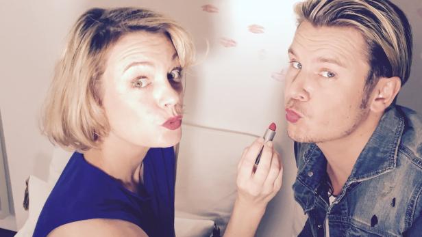 Eine Frau und ein Mann schminken sich gegenseitig mit rotem Lippenstift.