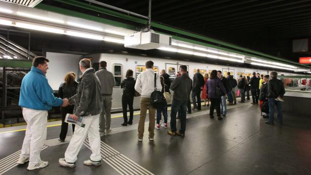 Menschen warten an einem Bahnsteig auf die einfahrende U-Bahn.