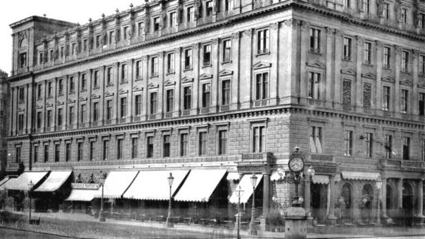 Ein historisches Foto eines großen Gebäudes mit Geschäften und einem Café im Erdgeschoss.
