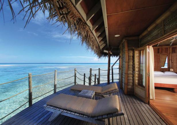 Blick von einer tropischen Hütte auf das türkisfarbene Meer mit zwei Liegestühlen auf der Terrasse.