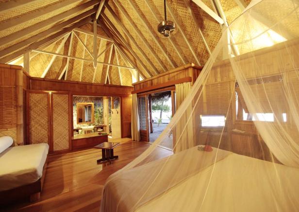 Ein Schlafzimmer mit Himmelbett in einem tropischen Resort mit Blick auf den Strand.