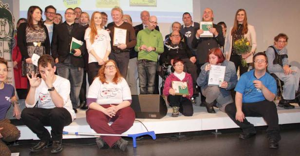 Eine Gruppe von Menschen mit und ohne Behinderung posiert auf einer Bühne mit Urkunden.