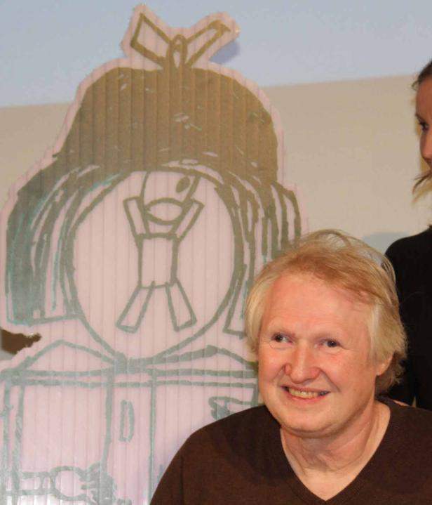 Ein lächelnder Mann mit blonden Haaren vor einer Pappfigur mit einer kindlichen Zeichnung.