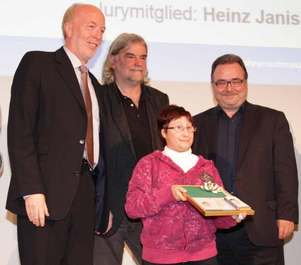 Eine Frau hält eine Auszeichnung, umgeben von drei Männern.