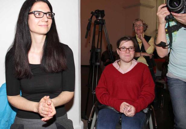 Eine Frau im Rollstuhl sitzt neben einer stehenden Frau mit Brille.