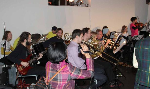 Ein Orchester spielt mit verschiedenen Instrumenten wie Trompeten, Posaunen, Geigen und Schlagzeug.