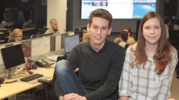 Ein junger Mann und eine junge Frau sitzen in einem Büro mit mehreren Arbeitsplätzen.