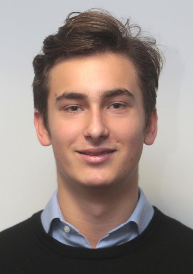 Ein junger Mann mit braunen Haaren und einem hellblauen Hemd lächelt.