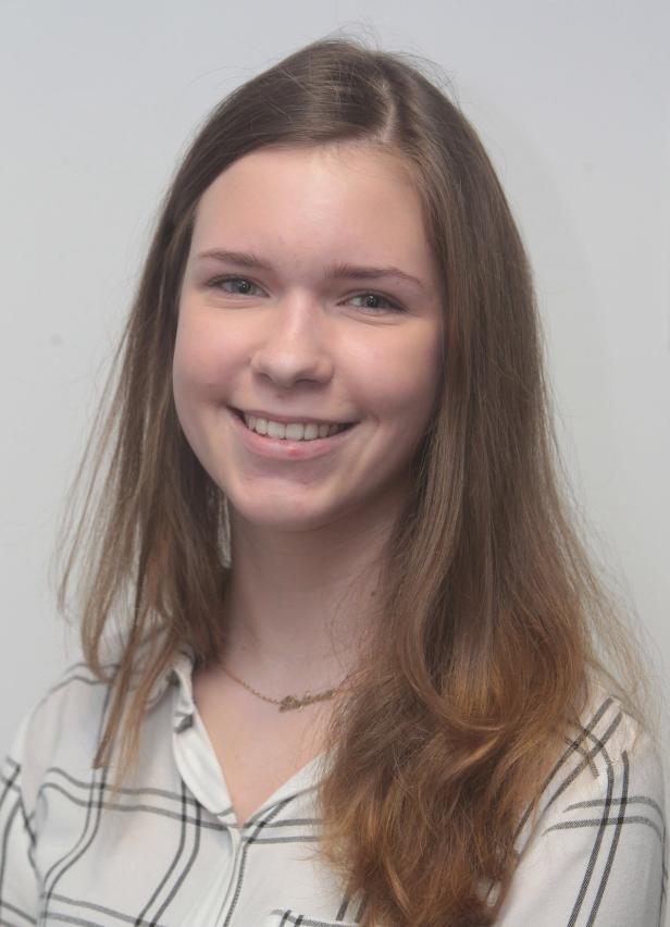 Eine lächelnde junge Frau mit braunem Haar und einem karierten Hemd.