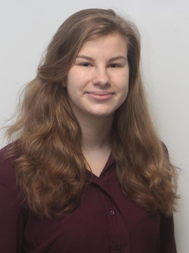 Porträt einer lächelnden jungen Frau mit langen, gewellten braunen Haaren.