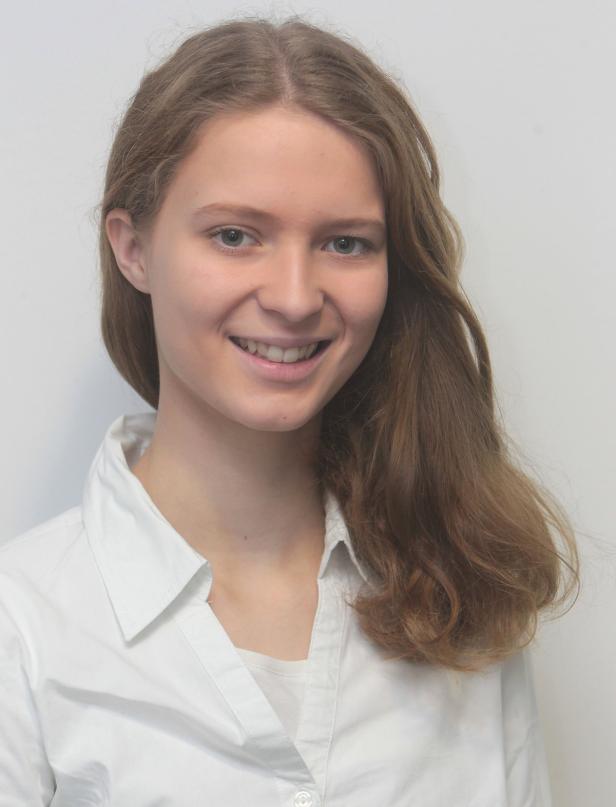 Eine junge Frau mit langen, gewellten Haaren lächelt in die Kamera.