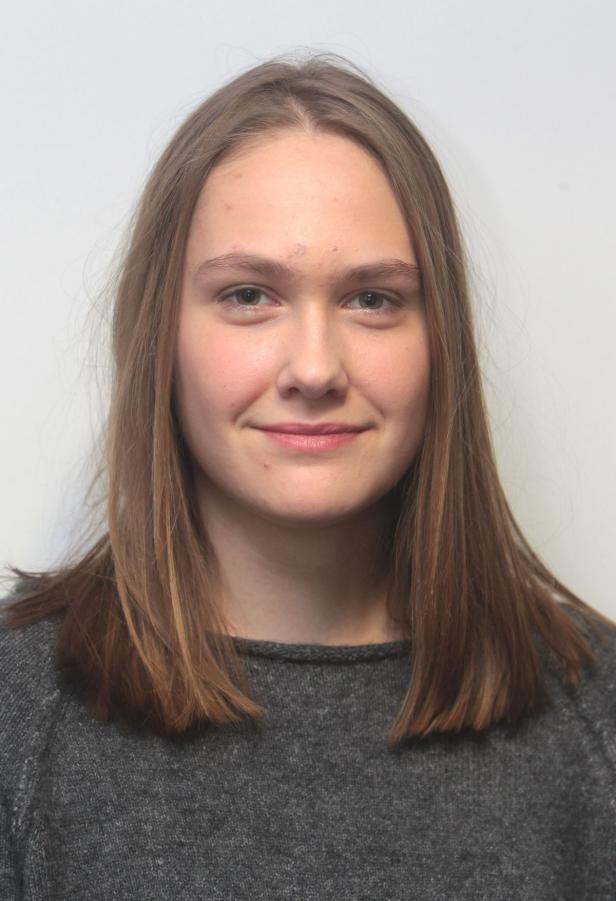 Porträt einer jungen Frau mit langen, braunen Haaren und einem grauen Pullover.