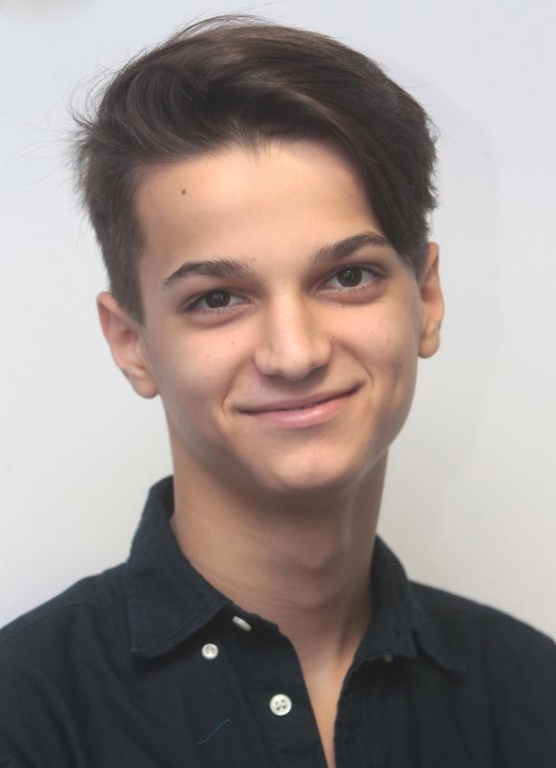 Ein junger Mann mit dunklen Haaren und einem schwarzen Hemd lächelt.